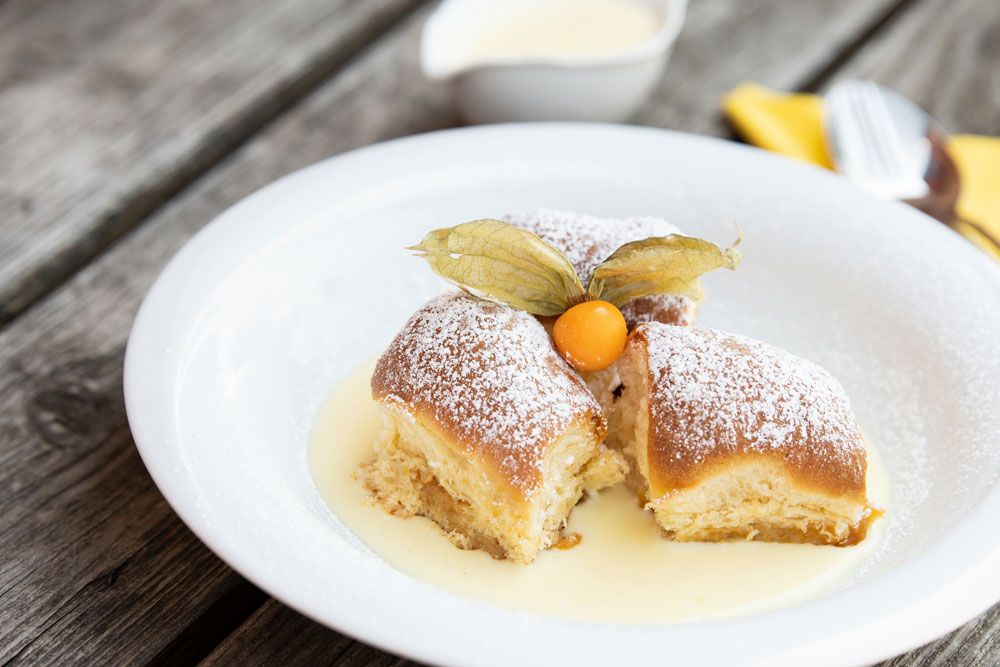 Three Buchteln with powdered sugar and physalis on vanilla sauce on a white plate.
