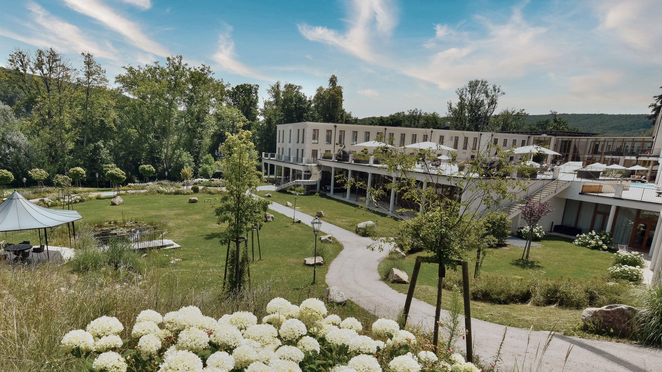 Ein modernes Gebäude mit Terrasse in einem grünen Park mit Blumen und Bäumen.