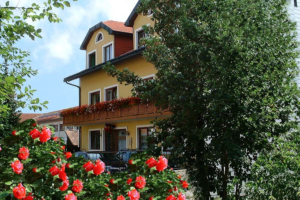 Gelbes Hotelgebäude mit Balkon, umgeben von blühenden roten Rosen und Bäumen.