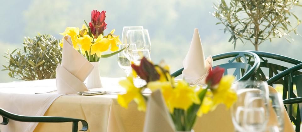 An elegantly laid outdoor table with yellow and red flowers, white napkins and wine glasses.