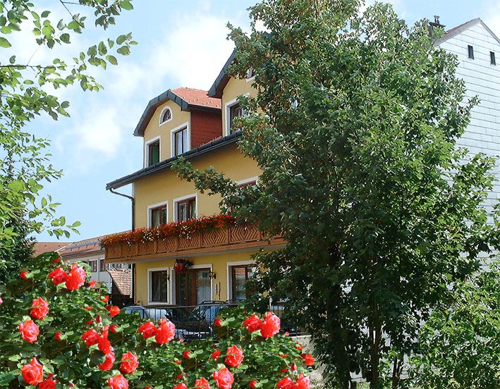 Ein gelbes, dreistöckiges Gebäude mit roten Rosen im Vordergrund und Bäumen an der Seite.