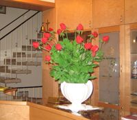 Ein Blumenarrangement mit roten Rosen in einer weißen Vase auf einem Tisch in einem Innenraum.