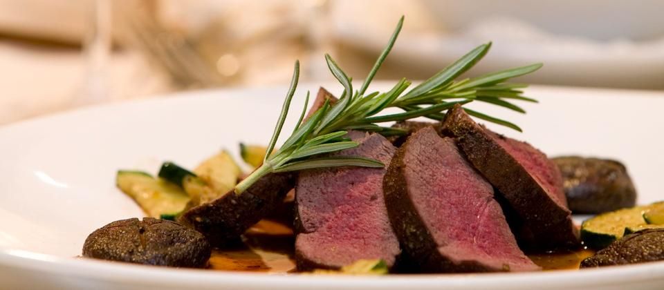 A gourmet dish with pink roasted meat, garnished with rosemary, on a plate with zucchinis and mushrooms.
