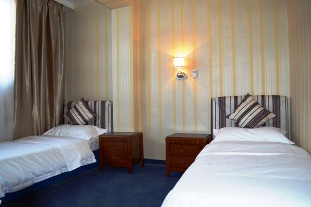 Ein Hotelzimmer mit zwei Einzelbetten, Nachttischen und einer Wandlampe.