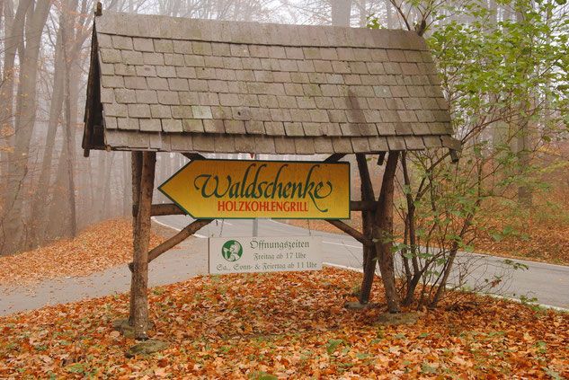 Ein hölzernes Schild im Wald weist zur Waldschenke Holzkohlengrill.