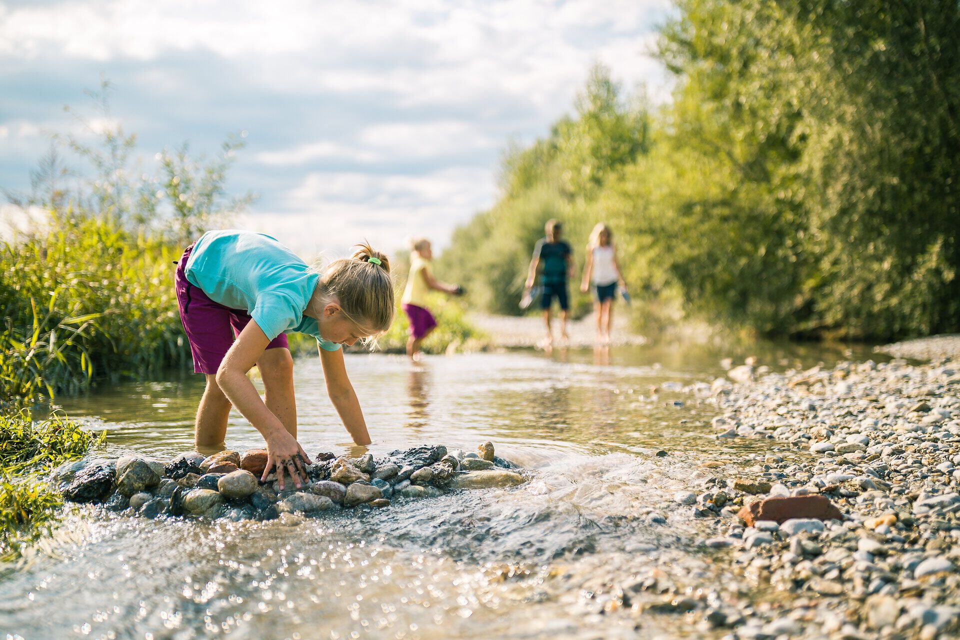 Ein Kind spielt mit Steinen im Flussbett der Leitha am Rosalia Rundwanderweg.