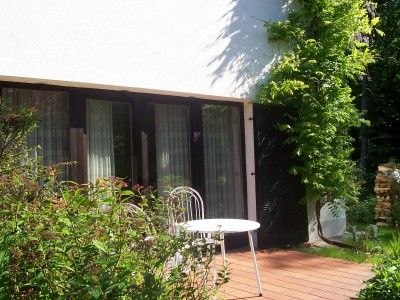 Terrasse mit Tisch und Stuhl vor einem Haus mit gro&szlig;en Fenstern.