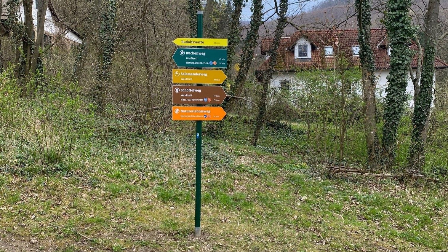 verschiedenfarbige Wegmarkierungen auf einem Metallsteher im Wald  