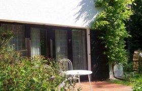 Terrasse mit Tisch und Stuhl vor einem Haus mit gro&szlig;en Fenstern.